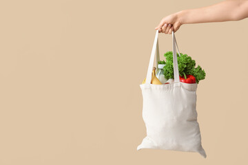 Female hand holding eco bag with different groceries on beige background © Pixel-Shot