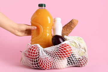 Female hand with vegetables and bottles of drinks in mesh bag on pink background