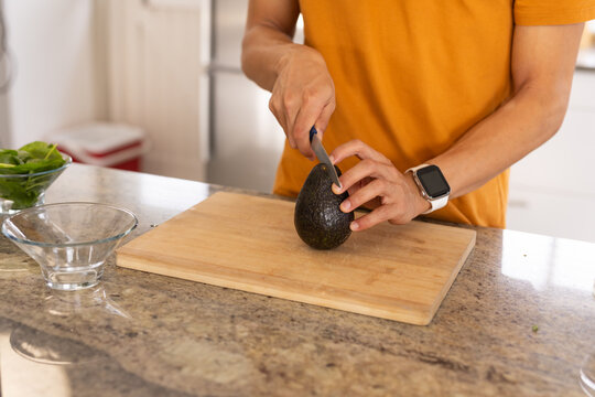 Avocado being sliced on wooden cutting board on speckled granite countertop near bowls
