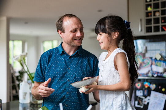 A man and a young girl enjoy a cheerful time in the kitchen washing dishes