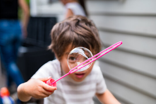 A young child plays with a bubble wand, creating large bubbles outdoors in a backyard setting