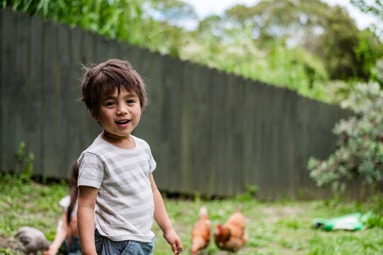 Happy child smiling while playing outside with hens in a garden area