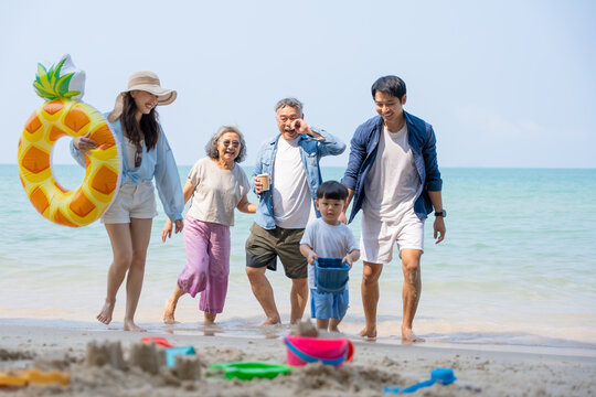 Multi-generational Asian family enjoying summer beach vacation together. Grandparents, parents, and child bonding by the sea, joyful outdoor. family, beach, vacation, summer, multi-generational.