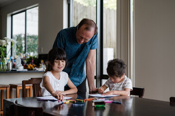 Children colour in while their father observes and encourages them in the kitchen