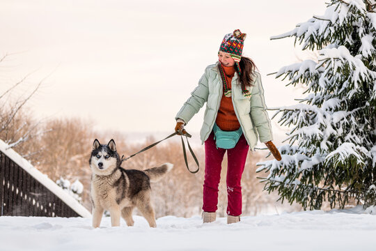 Asian woman walking a husky dog on a leash in a snowy winter