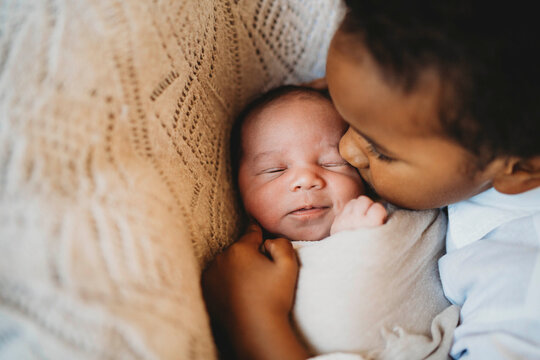 Multiracial boy kissing hugging smiley newborn baby in bed