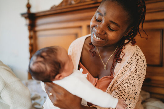 Black mom smiling holding multiracial newborn baby in bed
