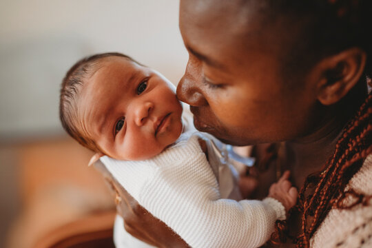 Black mom kissing multiracial newborn baby