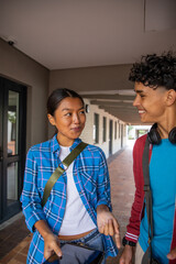 Diverse student friends walking and talking in campus corridor with tablet backpacks headphones © wavebreak3