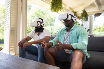 African american male friends using vr headsets and sitting on sofa under patio beams with plants © wavebreak3