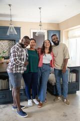 Fototapeta premium Diverse friends laughing while hugging each other in kitchen around island under glass pendants