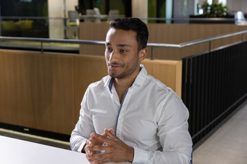 Obraz premium Indian man sitting at white desk in office reception wearing white shirt and dark trousers
