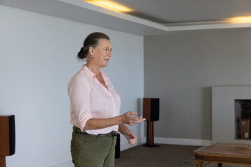 Naklejka premium Senior female standing in living room near fireplace, wooden speakers and coffee table, copy space