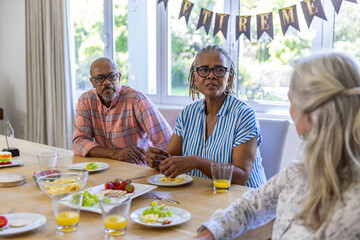 Diverse senior friends gathering at table sharing fruit and juice, celebrating retirement