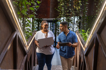 Diverse coworkers in business attire at office with led strips carrying laptop and tablet