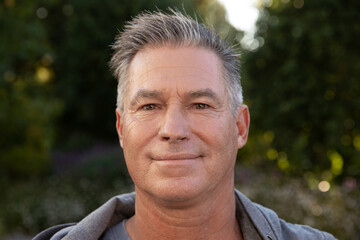 Middle-aged man standing calmly in backyard garden wearing hoodie under soft sunlight