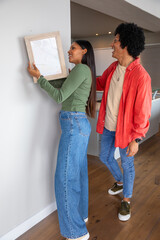 African american and indian couple hanging framed picture on white wall in kitchen area © wavebreak3
