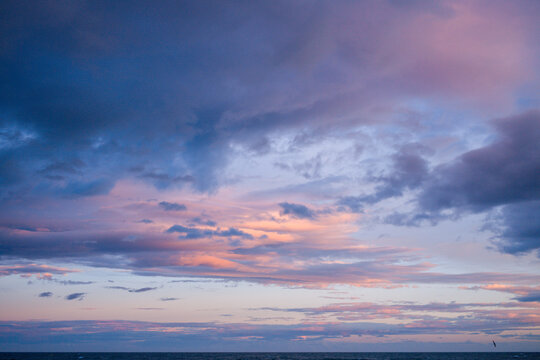 Vibrant layers of blue and pink clouds sweep across the sky above a calm Mediterranean Sea near Agde, creating a peaceful and expansive coastal scene at sunset.