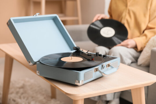 Young woman with vinyl disk in living room, focus on retro record player