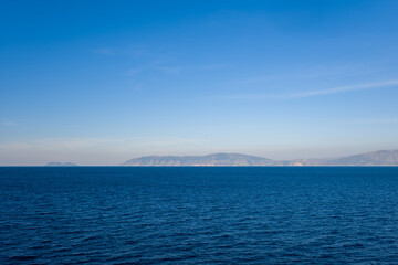 Obraz premium A wide expanse of deep blue water stretches toward a distant mountainous coastline under a clear blue sky. The scene captures the tranquil atmosphere and minimal composition of the Adriatic region.