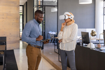 Diverse coworkers exploring vr demo at open-plan office next to paneled walls using tablet