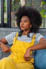Fototapeta premium African american woman sitting on sofa at home gazing through window beside headphones