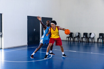 African american male basketball players in jerseys dribbling ball on court with water bottle
