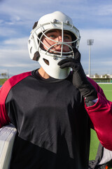 Obraz premium Field hockey goalkeeper adjusting helmet chin strap on turf under floodlights