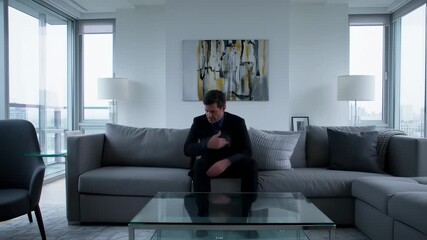 Stressed businessman in suit sitting on couch in modern apartment, concept of burnout