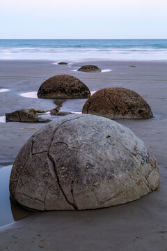 Moeraki boulders and ocean at dusk on beach.