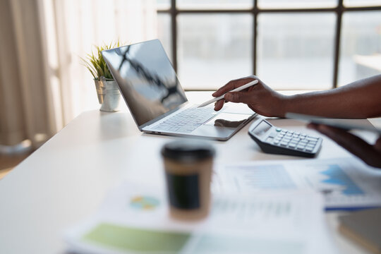 Professional hand using a digital pen on a laptop keyboard at a modern workspace, managing finance with a calculator and business documents illustrating reports and data - Powered by Adobe