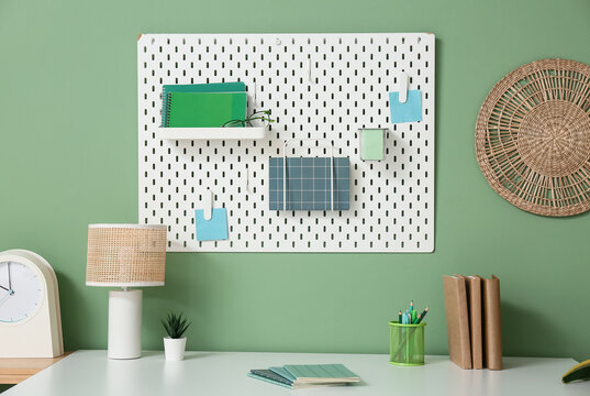 Comfortable workplace with stationery, lamp and pegboard on color wall