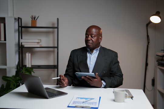 Senior african american businessman working in an office setting, analyzing financial reports and using a digital tablet with a stylus, demonstrating focus and expertise in data management - Powered by Adobe