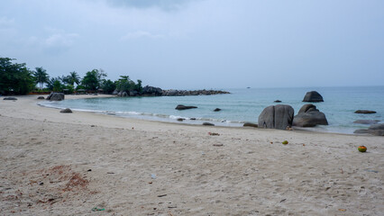 Scenic view of Siangau Beach in Bangka Island Indonesia featuring white sand calm turquoise water and iconic granite rock formations under a cloudy sky