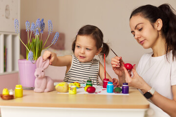 Happy mother and cute little child girl are preparing to celebrate Easter at home. Mom and daughter painting eggs before Easter together.