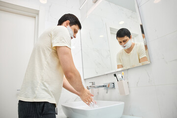 Man rinsing shaving cream from his face with water in a clean white bathroom sink
