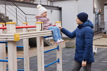 Dad and young girl interacting on playground during a casual autumn or winter day
