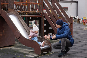 Father catching his toddler daughter sliding down a playground slide