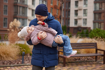 Father playing with happy daughter, having fun outdoors in warm winter clothing