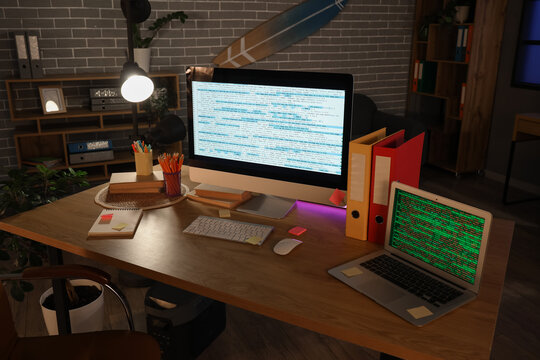 Computer monitor and laptop with codes on programmer's desk in dark office