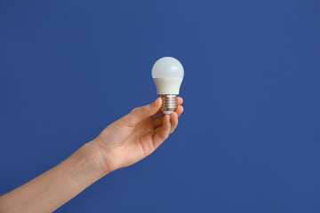 Female hand with white light bulb on dark blue background © Pixel-Shot