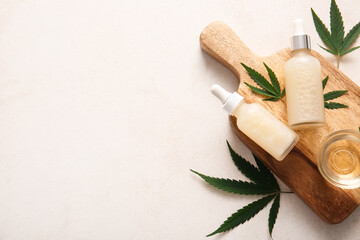 Bottles and glass bowl of hemp cosmetic oil with leaves on white background