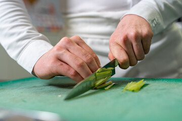 Gros plan sur les mains d’un chef coupant un légume sur une planche, avec le couteau en pleine...
