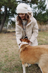 Obraz premium Woman in a warm coat and beanie crouches to greet a large dog, enjoying a playful moment outdoors in a park on a chilly day.