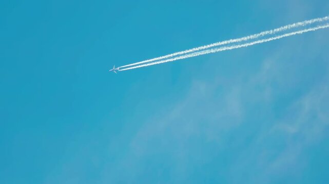 Passenger or cargo airplane flying in blue sky leaving chemtrail lines. Jet moving at high altitude creating atmospheric pollution and air contamination. Aviation activity impacting ecology and