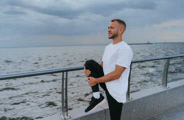A man holds a deep stretch, focusing on balance and breathing, on a walkway overlooking the river.