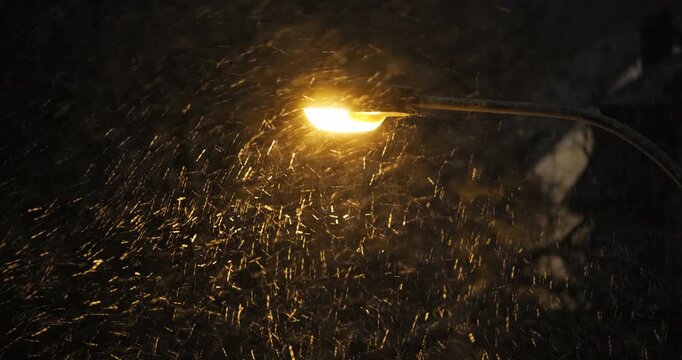 Street light illuminating falling snow during snowstorm at night. Above, close up, telephoto view, real time video, dark background, no people