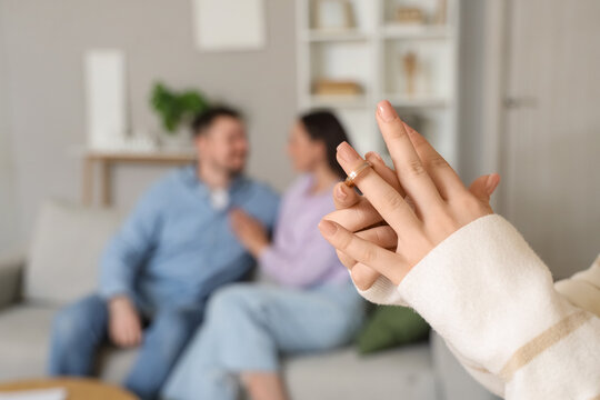 Young woman taking off wedding ring and her husband with mistress at home, closeup. Cheating concept