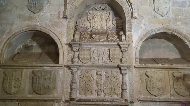 Tombs and Heraldic shields carved in stone. Medieval symbols. Panoramic view of a wall with feudal tombs and shields carved in stone and a stained-glass window with vibrant colors.