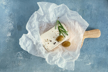 Paper with tasty feta cheese, olives, rosemary and peppercorn on blue background